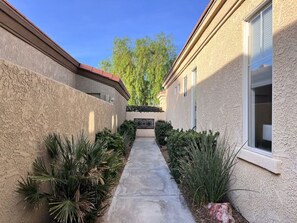 Een smal betonnen pad, begrensd door beplanting en gebouwen met stukwerk muren en ramen.