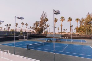 Una cancha de tenis exterior con varias canchas, palmeras y farolas.