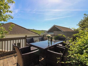 An outdoor patio with wicker furniture, a glass table, and a view of the surrounding landscape.