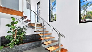 A modern staircase with glass railings and wooden steps, leading to a landing with a dark wood bench and a potted plant.