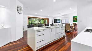 A modern kitchen with white cabinetry, a central island, and a dining area with a view of greenery.