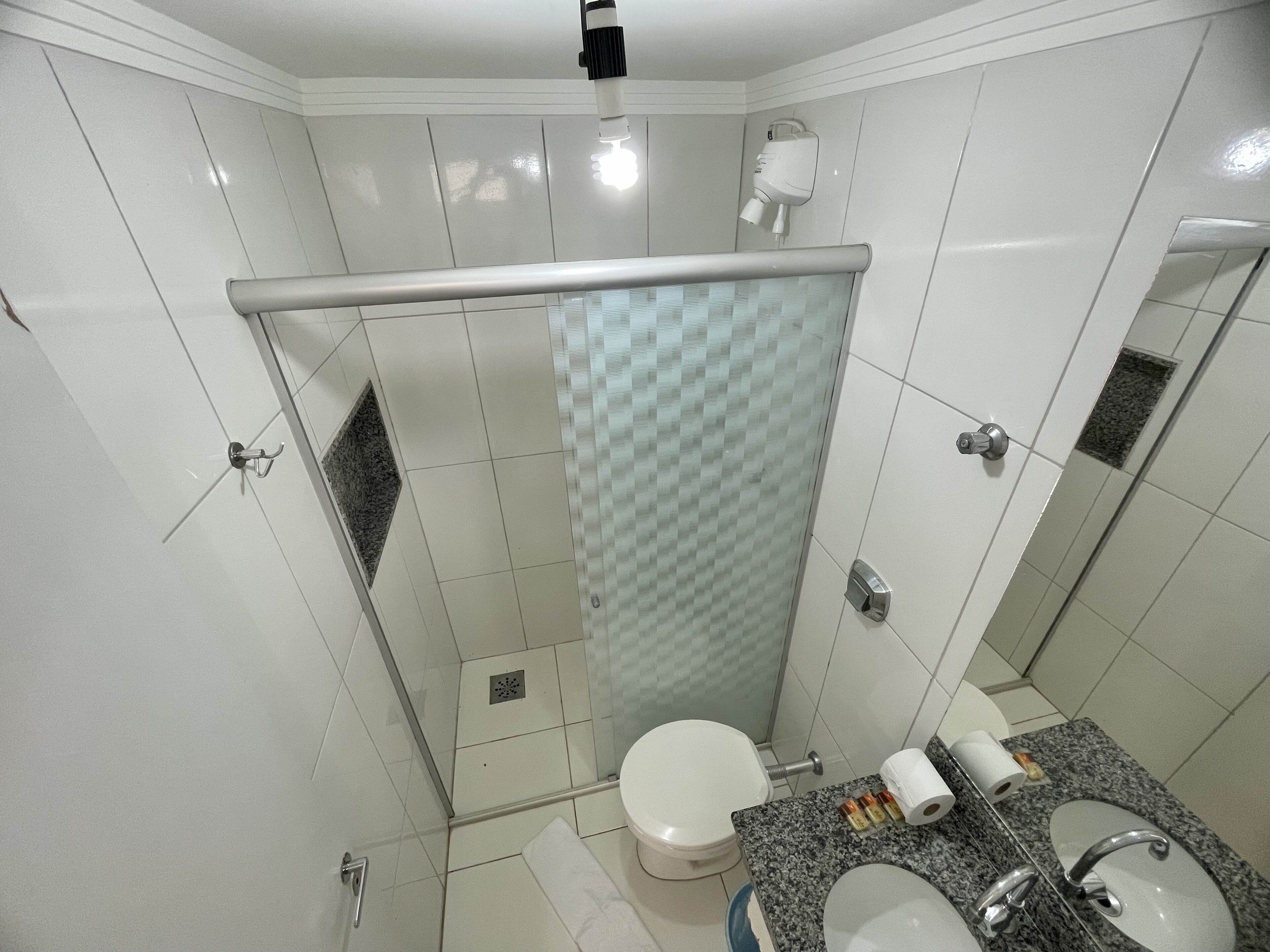 A modern bathroom with a glass shower enclosure, a toilet, a sink with a granite countertop, and a mirror.