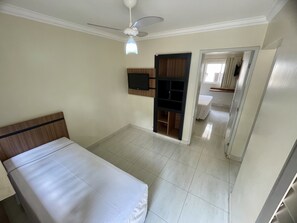 A bedroom with a bed, a ceiling fan, a TV mounted on the wall, and a door leading to a bathroom.