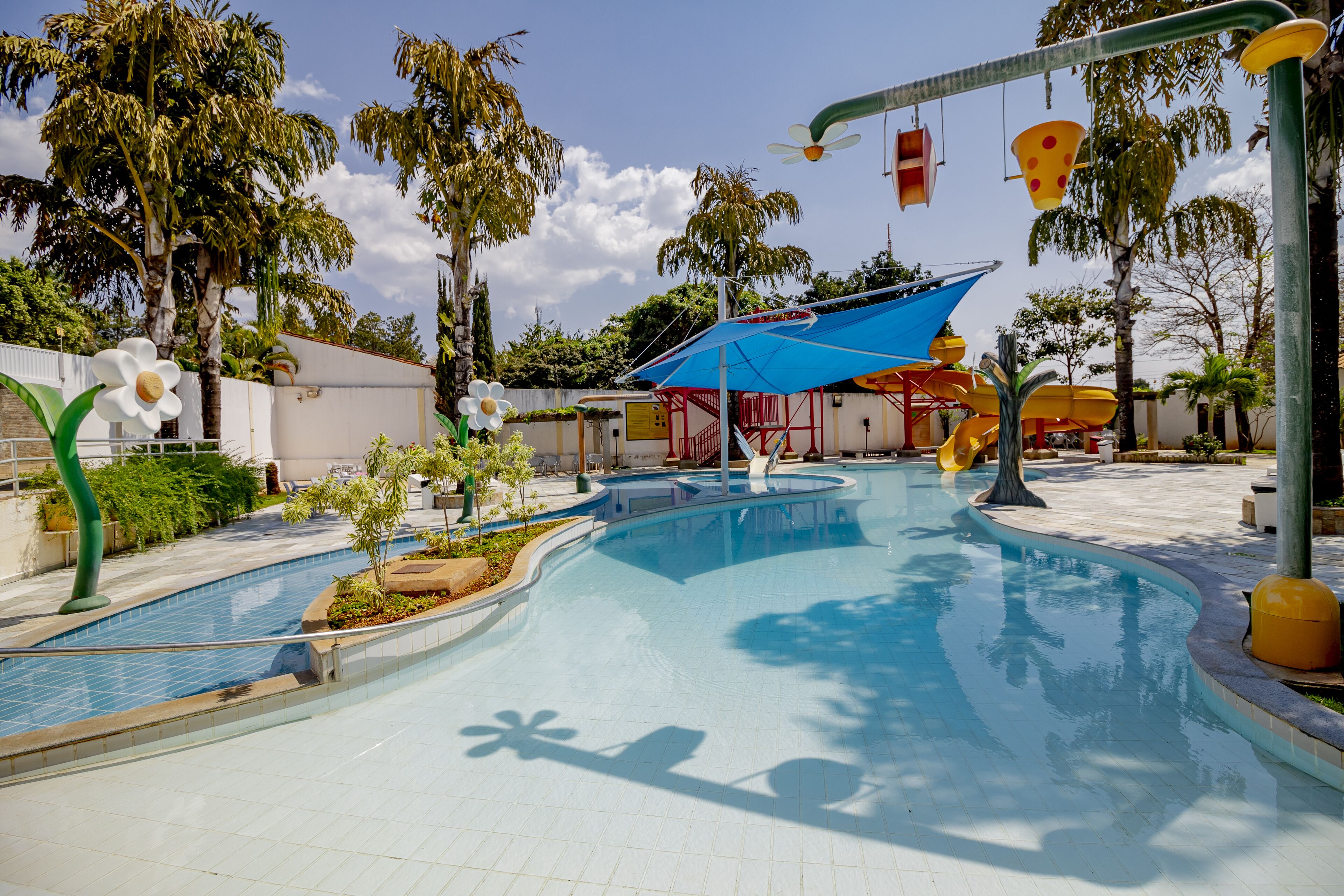 Une piscine dotée d’un auvent bleu, de palmiers et d’un toboggan.