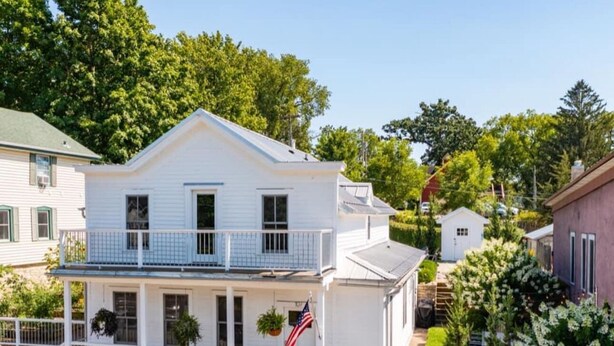 A two-story house with a balcony, a flag, and a stone wall.
