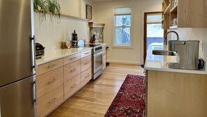 A modern kitchen with stainless steel appliances, wooden cabinets, and a red patterned rug.