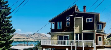 Una casa de dos pisos con balcón, chimenea y vistas a un lago y montañas.