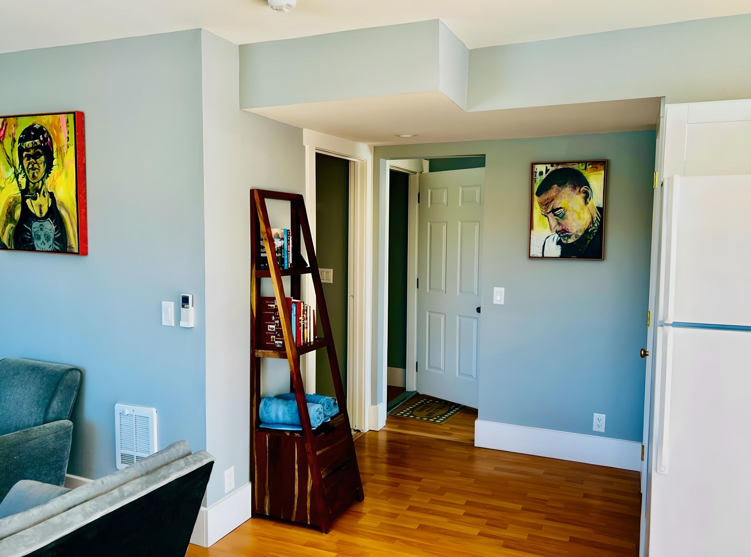 A hallway with a wooden floor, a bookshelf, and two paintings on the walls.