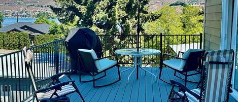 A deck with outdoor furniture, a grill, and a view of a town and mountains.