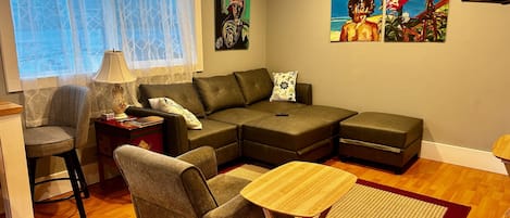 Uma sala de estar com sofá em forma de L, uma mesinha, uma poltrona e duas pinturas na parede.