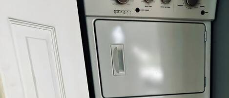 A compact, white Whirlpool stacked washer and dryer unit in a room with wooden flooring and a white door.