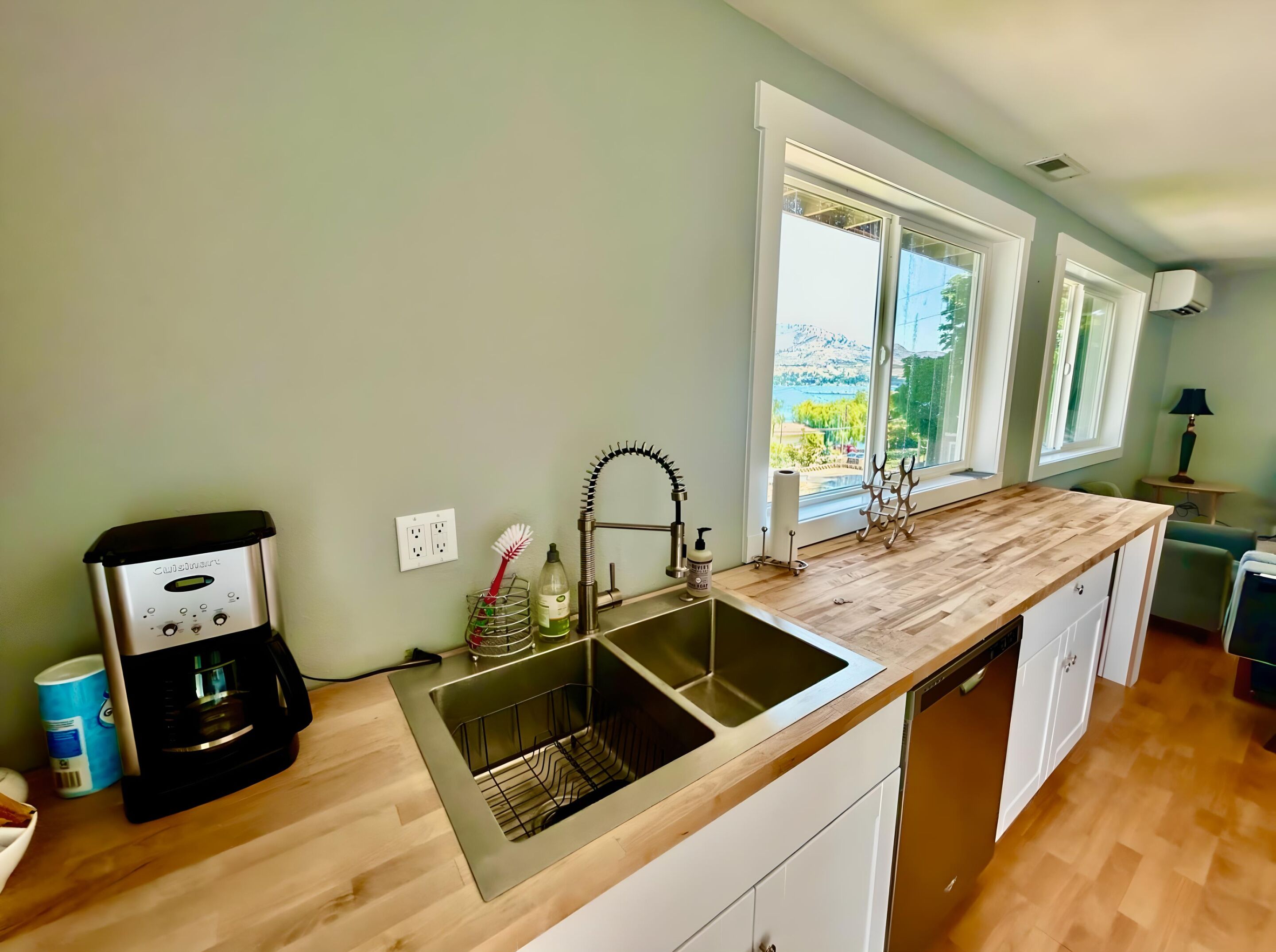A kitchen with a stainless steel sink, wooden countertop, and a view of a mountainous landscape through large windows.