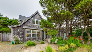 Ein Haus mit geneigtem Dach, einer Veranda und einem Garten mit verschiedenen Pflanzen und einem kleinen Teich.
