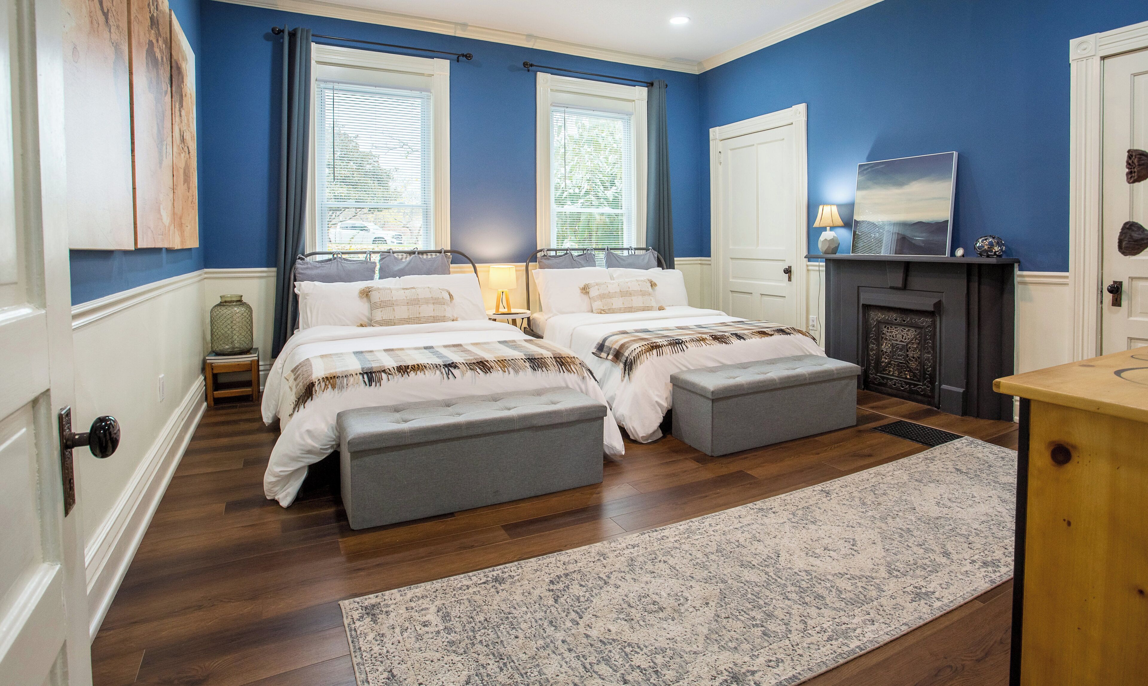 A bedroom with two beds, a fireplace, and a large window with blinds.