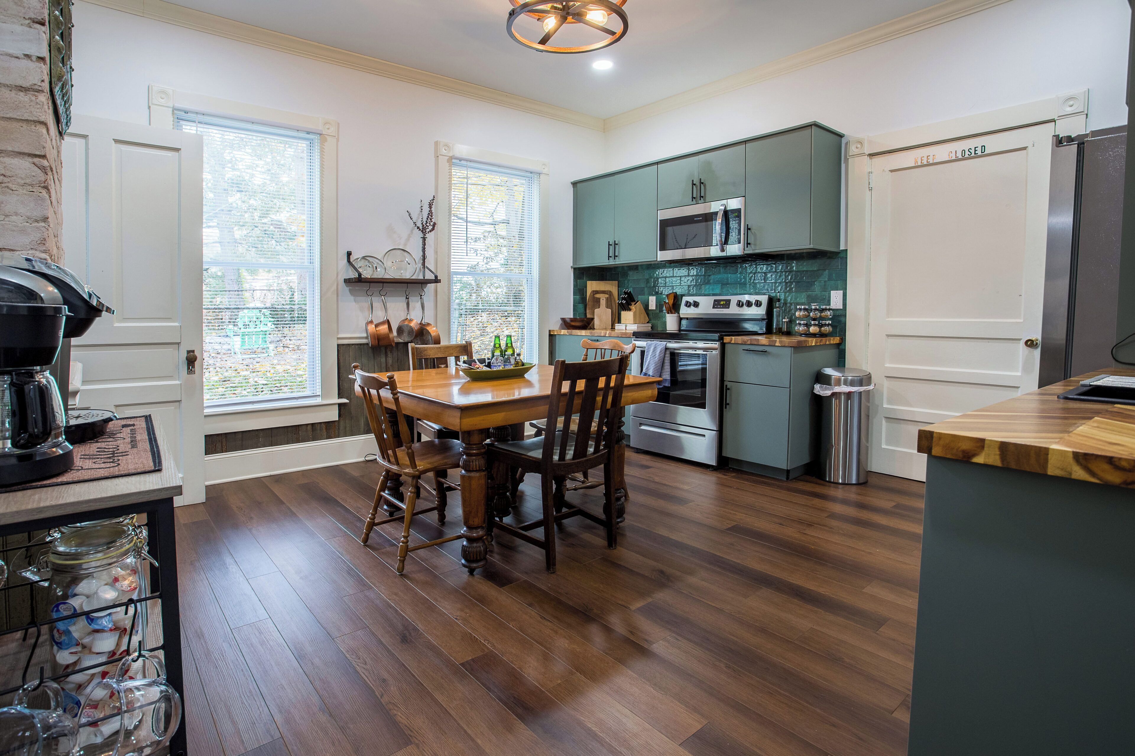 A kitchen with wooden flooring, a dining table with chairs, a stove, a microwave, and a refrigerator.