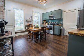Une cuisine avec un plancher en bois, une table à manger avec des chaises, une cuisinière, un four à micro-ondes et un réfrigérateur.