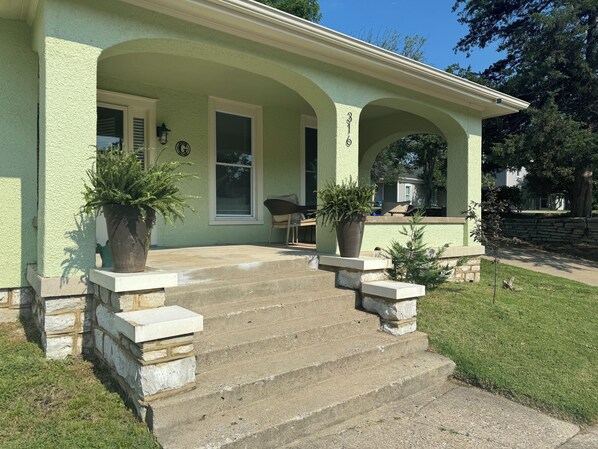 A house with a green exterior, a covered porch with steps, and two potted plants.