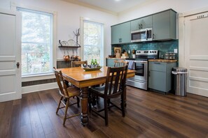 A kitchen with wooden flooring, a dining table with chairs, a microwave, an oven, and a trash can.