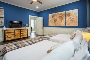 A bedroom with a large bed, a dresser, a flat-screen TV, and two wall-mounted maps.