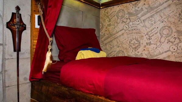 A room with a bed, a red curtain, a wooden headboard, and a wall with a map design.