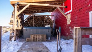 A wooden deck leading to a red building with a covered area and stacked firewood.