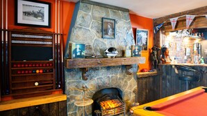 A billiards room with a stone fireplace, a pool table, and a bar area with memorabilia.