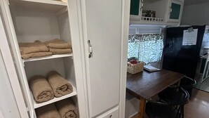 Eine kleine Küche mit einem Holztisch, zwei schwarzen Stühlen und einem weißen Schrank mit Handtüchern.