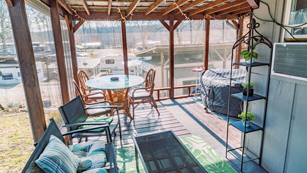 Eine überdachte Terrasse im Freien mit Tisch und Stühlen, einer gepolsterten Sitzecke und einem Metall-Pflanzgefäß.