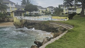 A coastal area with a white bridge, rocky shoreline, and a grassy path leading to a white structure. - Apartment E6 (Tower Isle)
