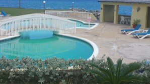 A swimming pool with a white fence, lounge chairs, and a view of the ocean. - Apartment E6 (Tower Isle)
