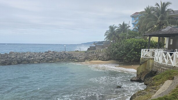 A coastal view with a rocky breakwater, a sandy beach, and a small structure with a white railing. - Apartment E6 (Tower Isle)