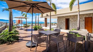 A wooden deck with outdoor furniture, palm trees, and a view of the ocean.