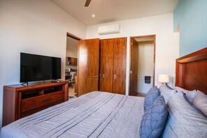 A bedroom with a bed, a TV, wooden wardrobes, and an air conditioning unit.