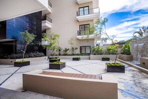 A modern outdoor courtyard with multiple planters, a central seating area, and a building with balconies. - Rooftop Views + Gym + Parking | 2BR in Versalles (Puerto Vallarta)