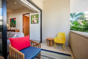 A balcony with a sofa, a yellow chair, a small table, and a view of greenery. - Rooftop Views + Gym + Parking | 2BR in Versalles (Puerto Vallarta)
