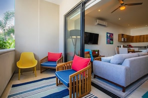 A living room with a sofa, chairs, a TV, and a kitchen area.