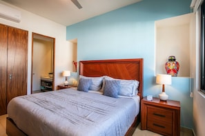 A bedroom with a large bed, wooden headboard, two bedside tables with lamps, a wardrobe, and a decorative vase. - Rooftop Views + Gym + Parking | 2BR in Versalles (Puerto Vallarta)