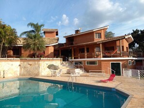 Ein zweigeschossiges Haus mit Swimmingpool, einer überdachten Terrasse und einer Ziegel Fassade.