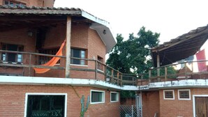 A two-story brick building with a balcony, a small garden area with a lawn and a few chairs, and a metal gate.