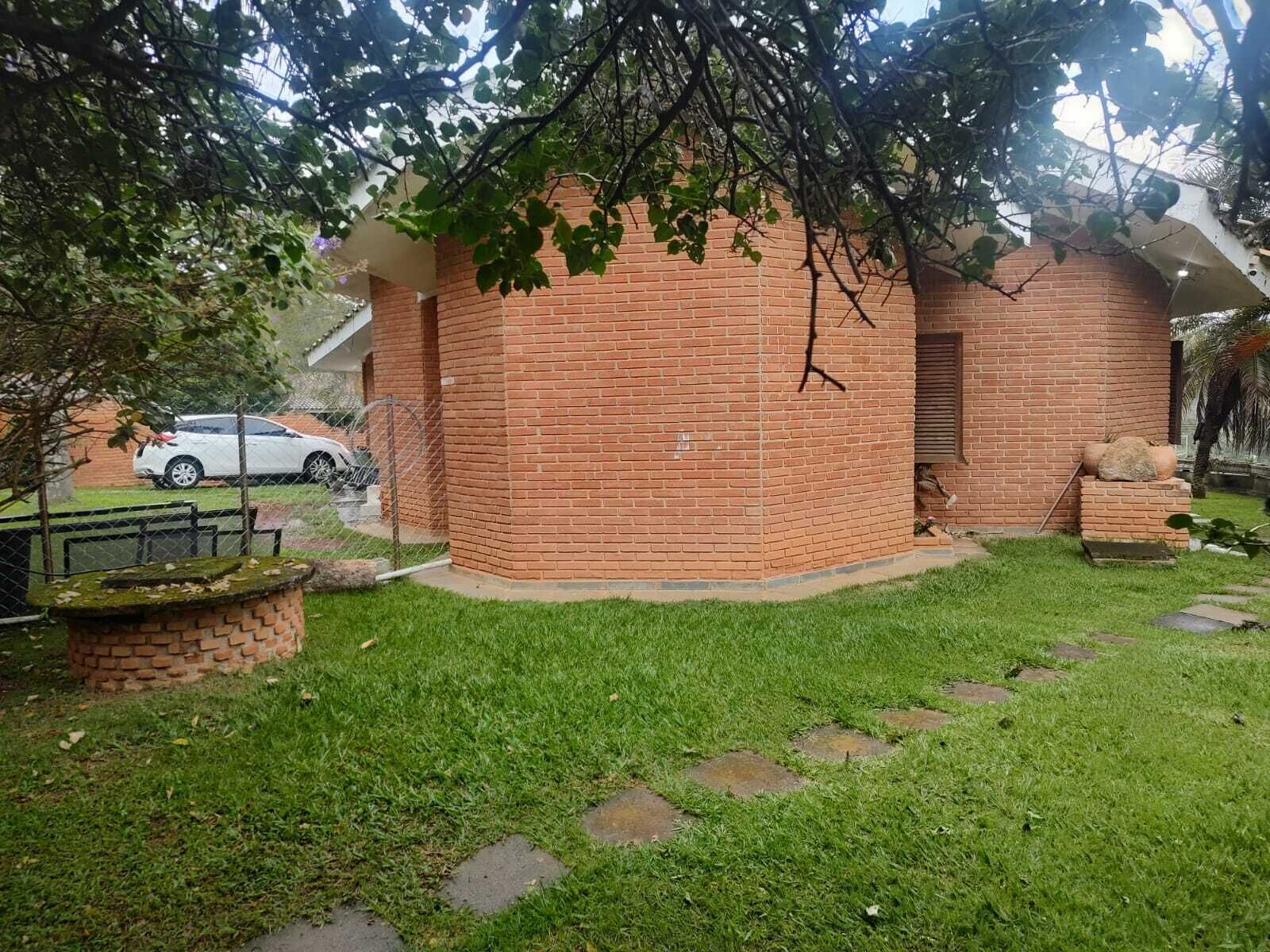 A brick building with a small garden area, a paved walkway, and a white car parked in the background.