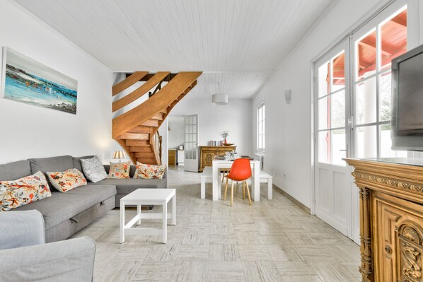 A spacious living room with a grey sofa, white coffee table, and a wooden staircase leading to an upper level. - House for 10 - garden - 600 m from the beach (Andernos-les-Bains)