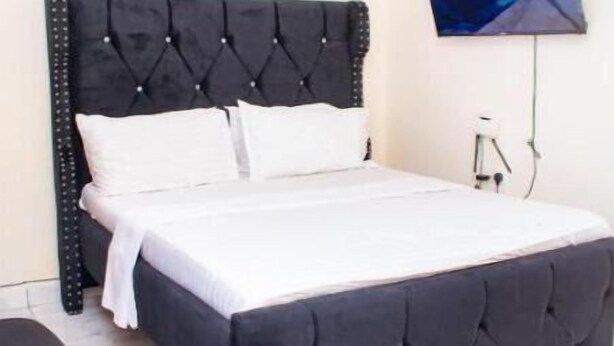 Une chambre à coucher avec une tête de lit noire à motifs capitonnés, du linge de lit blanc et un téléviseur à écran plat fixé au mur.