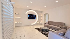 A modern living room with a curved wall, a flat-screen TV mounted above a sofa, and a minimalist design with recessed lighting.