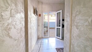 A narrow hallway with a tiled floor leading to a glass door opening to an outdoor area.
