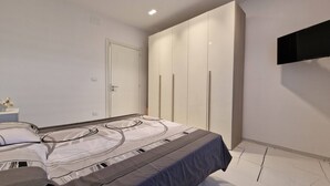 A modern bedroom with a large bed, a wardrobe, and a flat-screen TV mounted on the wall.