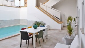 A modern indoor pool area with a white table and chairs, a staircase, and potted plants.
