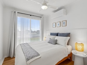 A bedroom with a bed, a bedside table with a lamp, a ceiling fan, and a window with curtains. - Coastal Break - Family Escape in Port Hughes (Port Hughes)