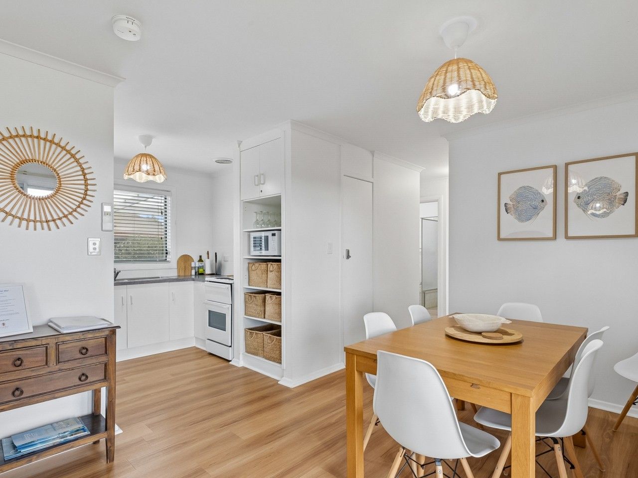 Une cuisine moderne avec des meubles blancs, une table à manger en bois, des chaises blanches et un luminaire suspendu.