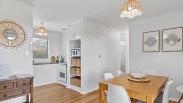 Une cuisine moderne avec des meubles blancs, une table à manger en bois, des chaises blanches et un luminaire suspendu.