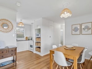 A modern kitchen with white cabinets, a wooden dining table, white chairs, and a hanging light fixture. - Coastal Break - Family Escape in Port Hughes (Port Hughes)